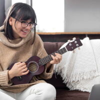 Young stylish girl with glasses learns to play the ukulele. Concept of online education, home education.